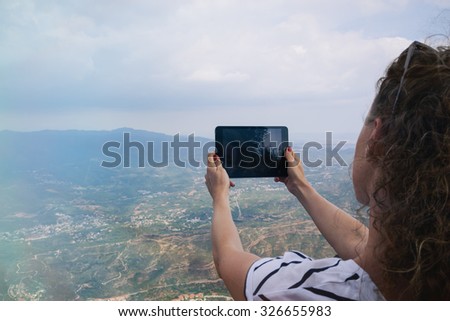 Female tourist takes photos with her digital tablet on peak of rock