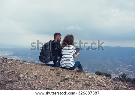 Young tourists with backpacks enjoying and shooting valley view on a digital tablet  from top of a mountain