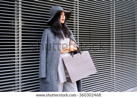 young beautiful stylishly-dressed Asian girl posing and holding a blank paper bag with empty space for your text or logo