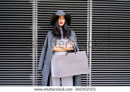 young beautiful well-dressed Asian girl posing and holding a blank paper bag with empty space for your text or logo