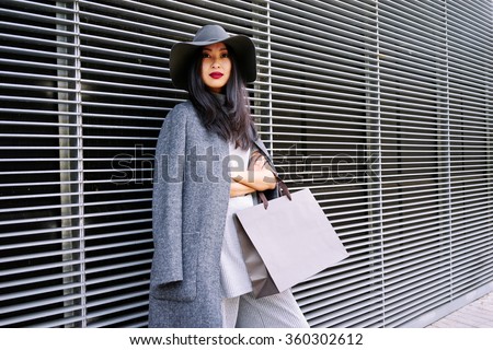 young attractive stylishly-dressed Asian girl posing and holding a blank paper bag with empty space for your text or logo