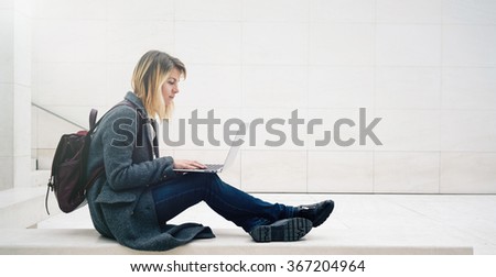 young attractive blonde female student learning on-line on her laptop while sitting on the stone bench.copy space area for your text message or content