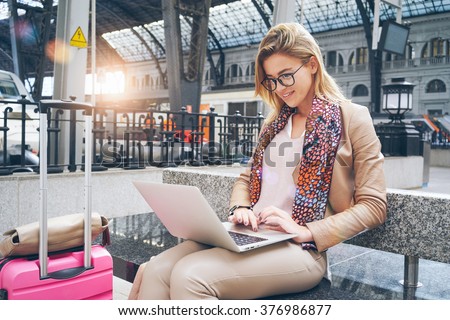 Beautiful Caucasian woman using net-book while sitting in train station interior. modern businesswoman using a laptop computer while waiting for the train. Flare light.