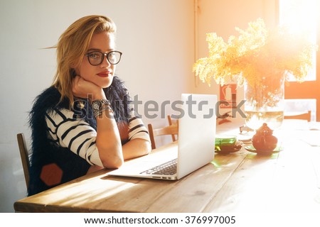 Portrait of attractive smiling female student posing while resting after work on her portable laptop computer during coffee break. flare light