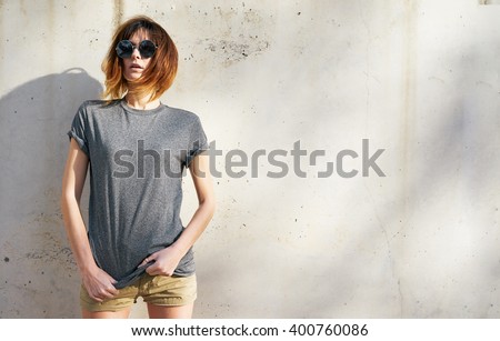 attractive young woman wearing in a gray blank t-shirt posing on a background of a concrete wall in the rays of the setting sun