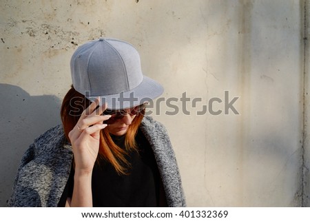 Portrait of a young attractive girl with cap. Female model wearing a gray blank cap and sunglasses looking away.