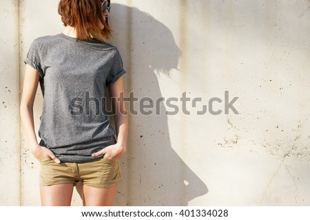 attractive young woman dressed in a gray blank t-shirt posing against a background of a concrete wall in the rays of the setting sun
