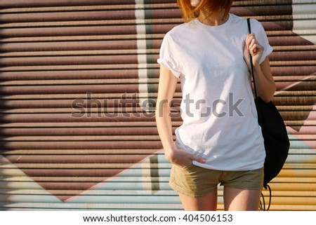 young girl with a backpack wearing a white blank t-shirt standing on a graffiti wall background