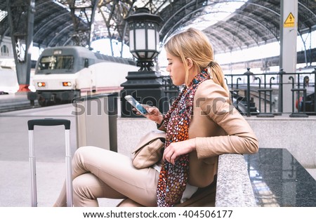 young attractive businesswoman writes a text message while waiting for the train. attractive young blonde woman using smart-phone while sitting on the railway station platform