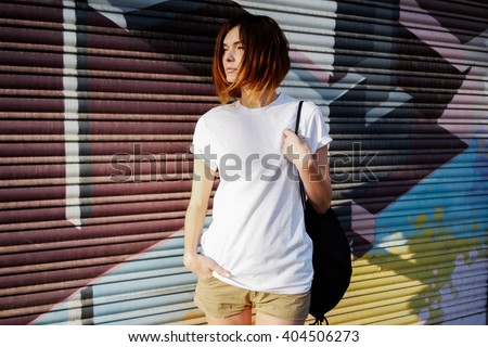 young attractive girl with a backpack wearing a white t-shirt standing on a graffiti wall background