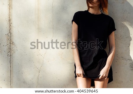 young girl wearing in a black blank t-shirt standing on a background of concrete wall. Sun rays