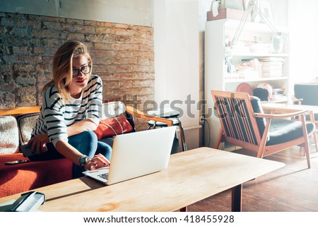 Beautiful young blonde female student using portable laptop computer while sitting in a vintage coffee shop.Young beautiful girl using a personal laptop computer to look up information on the internet