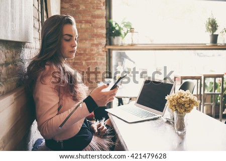 beautiful girl successful freelancer using laptop computer and writes a text message on your phone while sitting in coffee shop.attractive woman reading text message on cell telephone in cafe.