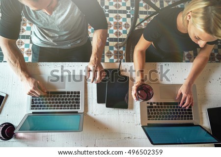 Young blonde woman and young man are sitting behind the laptops with blank screens. Co-workers are working together on a portable computers in a modern light office. View from the top.