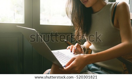 A cropped photo of a young female student with long brown hair studying online. Focus on the female hands typing on a keyboard of a portable computer. Flare light.