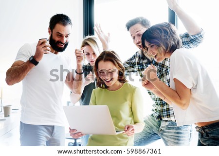 Happy business people celebrate the successful project realization while looking at laptop screen in the office. Successful corporate team of partners and coworkers are  excited with the victory.