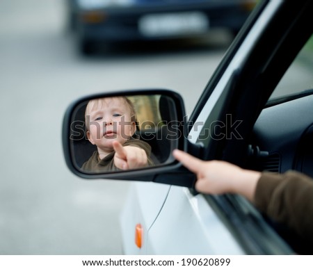 Small boy looking at his reflection in a car  mirror.