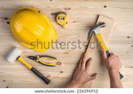 tools and hands working with hammer and helmet on wooden background