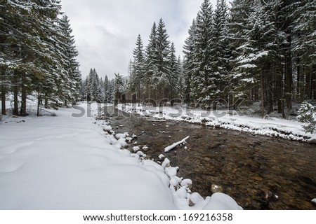 Winter landscape in a mountain valley with mountains stream