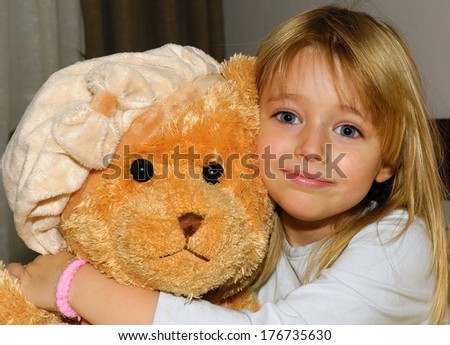Cute little happy girl hugging big brown teddy bear and sitting