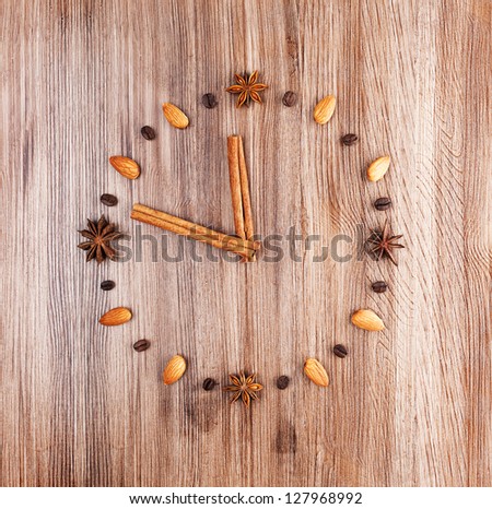 Time to cook. Clock face on a wooden background of almonds and coffee beans with arrow of cinnamon sticks.