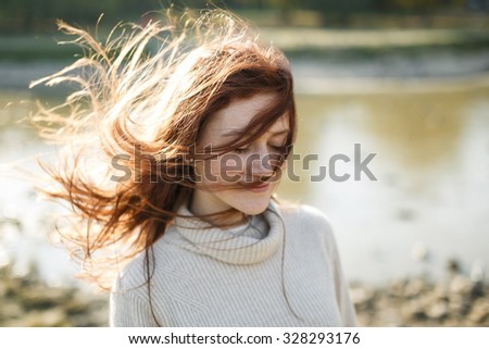 Portrait of a young funny happy redhead woman on the beach with flying hair in the wind outdoors. Young casual girl with wavy hair