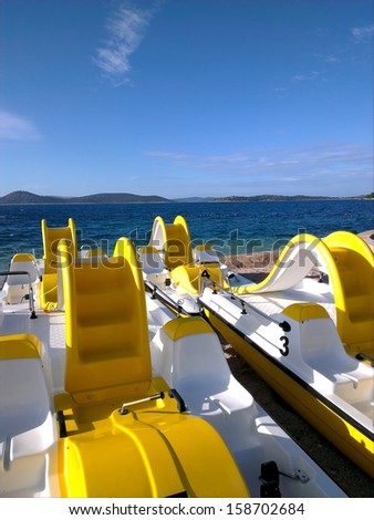 Few yellow/white pedal boats for rent on the blue sea line and clear blue sky/Pedal boats