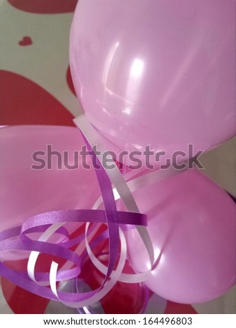 Close view on purple and silver ribbons and pink balloons as the decoration on the gift wrapped in paper colored with red hearts/Ribbon and balloon decoration