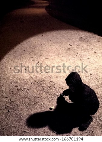 Kid and his shadow under the spotlight drawing in the sandy surface of the winding road to the dark/Spotlight of life