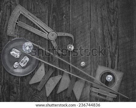 black and white image of a vintage jeweler tools and diamonds over wooden bench, space for text