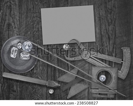 black and white image of a vintage jeweler tools and diamonds over wooden bench, blank card for your business