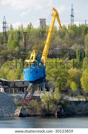yellow port crane on a river bank ready to load rocks