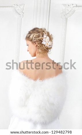 The young woman stands  turned  back. Her shoulders are covered with white fur mantle.Hairdress is decorated with  flower composition