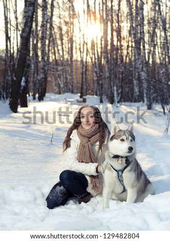 The young beautiful woman sits with husky dog in the winter forest