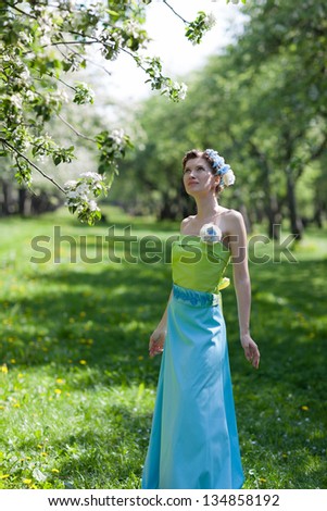 Beautiful young  woman in the spring garden stands near blossoming tree. Coiffure   is decorated with flowers.