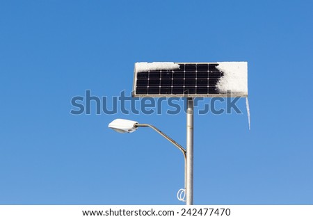 Solar powered street light with snow and ice on blue sky background