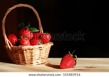Wicker basket full of strawberries on wooden surface under sunbeam. Good background with free space for text
