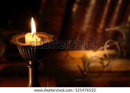 Vintage still life with lighting candle on background with old spectacles and books