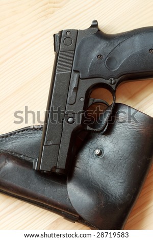 Modern automatic pistol and old leather holster on wooden background