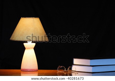Luminous table lamp standing near spectacles and books on dark background