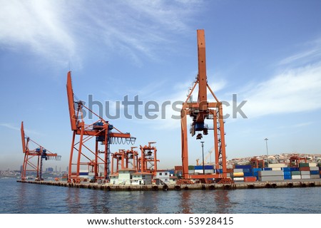 Panorama with blue sky, sea and container harbour. Closeup of few red cranes