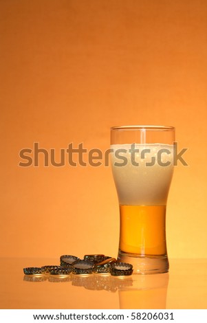 Bottle caps lying near glass of light beer with foam