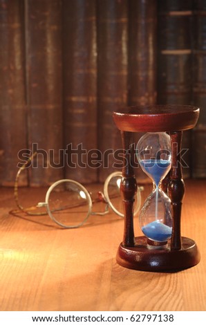 Vintage hourglass on background with old spectacles and books