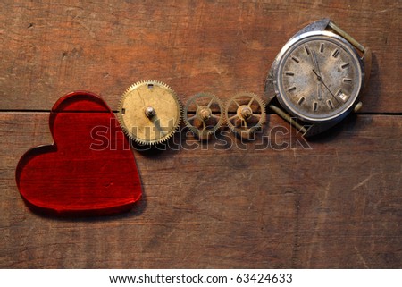 Red glass heart near gears and old watch on wooden background