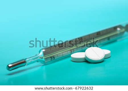 Stack of pills near clinical thermometer on green background