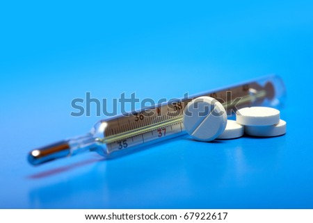 Stack of pills near clinical thermometer on blue background