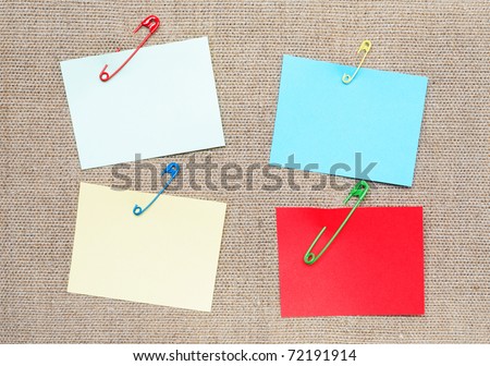 Blank color adhesive notes attached with safety pins to canvas background