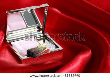 Open box with pink rouge and makeup brush on beautiful red silk
