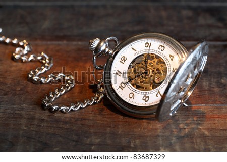 Vintage pocket watch with open lid and chain on wooden surface