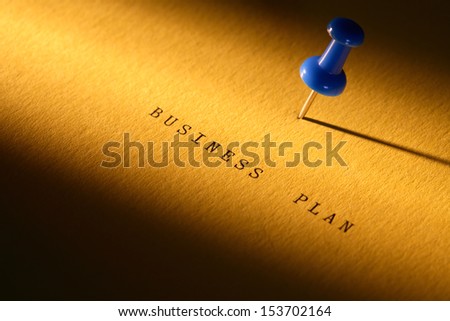 Business concept. Thumbtack on paper surface with BUSINESS PLAN inscription